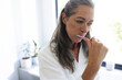 © Wavebreak Media - At home, mature Caucasian woman brushing teeth in a white robe