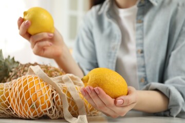 Wall Mural - Woman with lemons and string bag of fresh fruits at light table, closeup