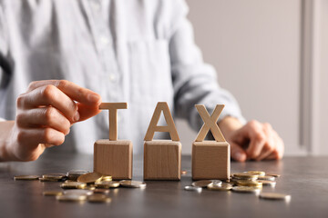 Wall Mural - Woman with word Tax, wooden cubes and coins at grey table, closeup