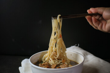 Wall Mural - Noodle with Kao Lao Moo Toon. Thai pork stew soup in white bowl on black table. Street food in Thailand.