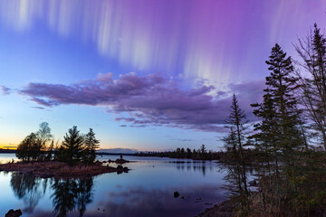 northern lights erupt over a lake in minnesota in a dark sky overhead shining rainbow of aurora ligh