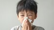 Health in Focus: Young Boy Blowing His Nose with a Tissue Against a White Background, Perfect for Educational Health Messages