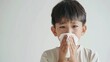Health in Focus: Young Boy Blowing His Nose with a Tissue Against a White Background, Perfect for Educational Health Messages