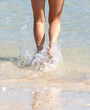 Legs of a girl walking on the water on the sandy beach of the sea