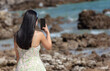 A girl in a dress photographs the sea. Back view