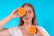curvy woman covering eye with piece of orange on blue background. concept of diet and healthy lifestyle	