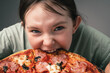 A little girl takes a bite out of a large pizza. Crazy little girl bites into pizza and looks close-up at the frame.