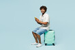 © ViDi Studio - Full body traveler Indian man wears white casual clothes sit on bag using mobile cell phone isolated on plain blue background. Tourist travel abroad in free time rest getaway. Air flight trip concept.