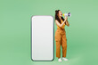 © ViDi Studio - Full body young woman wear yellow tank shirt top big huge blank screen mobile cell phone smartphone with copy space area scream shout in megaphone isolated on plain green background Lifestyle concept