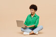 © ViDi Studio - Full body happy young IT woman of African American ethnicity wear green shirt casual clothes sit hold use work on laptop pc computer isolated on plain pastel light beige background. Lifestyle concept.