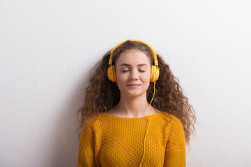 Poster - Portrait of a gorgeous teenage girl with curly hair, listening music via headphones. Studio shot, white background with copy space