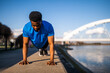 Young african-american man is exercising in the city. He is doing push-ups.