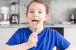 Happy little girl holding a fork in her mouth. A pre-teenage girl has breakfast in the kitchen at home with a plate of waffles, vegetables and cheese. Selected focus.