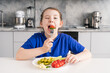 Funny little girl holding tomato and cheese fork in her mouth. A young girl is having breakfast in the kitchen. Selected focus. The concept of a healthy breakfast.