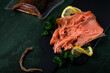 Hot smoked trout fillet served on the black board with lemon and parsley and a vacuum packed piece