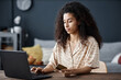 © AnnaStills - Young biracial woman sitting at desk in living room at home paying for goods in online store on laptop with bank card