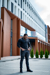 Wall Mural - A man in a black shirt and jeans stands in front of a building. The building is a large, modern structure with a white facade.
