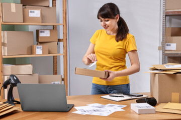 Poster - Parcel packing. Post office worker sticking barcode on box at wooden table indoors