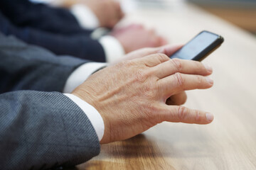 Man in a business suit uses a mobile phone - a smartphone, sitting next to colleagues during a business meeting or negotiations. Unrecognizable, without a face. Photo. Selective focus