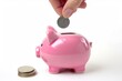 Hand holding a cent coin near a pink piggy bank, putting a coin into it, isolated on a white background.