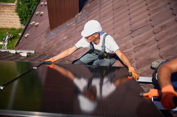 Wall Mural - Worker building solar panel system on rooftop of house. Man engineer in helmet installing photovoltaic solar module outdoors. Alternative, green and renewable energy generation concept.