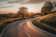 The warm glow of golden hour illuminating a winding rural road lined with trees. The minimalist composition, with just the road and colorful sky, conveys a sense of journey and adventure