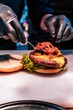 © Wirestock - Vertical shot of chef hands in black gloves putting the ingredient in burger