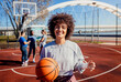 Portrait of young woman on basketball court looking at camera and holding ball in her hands.