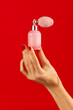 Unrecognizable woman hand holding perfume bottle on red backdrop