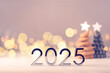 Metal numbers 2025 on a white table with Christmas trees and bokeh lights. Happy New Year 2025 is coming concept.