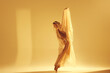 © master1305 - Dance of light. Artistic female ballet dancer in flowing golden dress making creative graceful performance against sand color background. Concept of art, classical dance, beauty, fashion, aesthetics