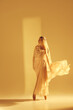 © master1305 - Ethereal beauty. Mystical scene of female ballet dancer with golden flowing fabric performing, symbolizing purity and elegance of ballet. Concept of art, classical dance, beauty, fashion, aesthetics