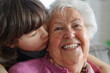 Cute girl hugging and kissing gradmother on cheek from behind. Portrait of an elderly woman spending time with granddaughter.