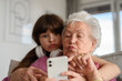 Grandmother with cute girl taking selfie with smartphone, making funny face. Portrait of an elderly woman spending time with granddaughter.