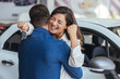 Happy couple buying a car at the dealership and holding the keys. Family celebrating buying a car at a car dealership. Happy couple hugging after buying a car at the dealership