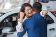 Happy couple hugging after buying a car at the dealership. Excited couple celebrating after buying a car at the dealership - car ownership concepts.