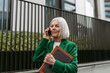 Mature businesswoman phone calling smartphone, going on business meeting in the city. Beautiful older woman with gray hair standing on city street.