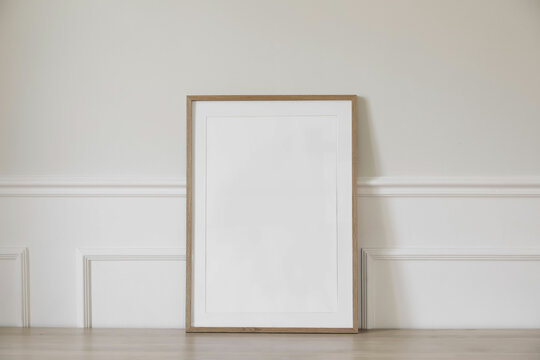 Minimal empty vertical wooden picture frame mockup. White wall with elegant stucco decor. Portrait large poster a3, a2 mock-up. Wooden table. Modern, minimal design. Scandinavian indoor interior.