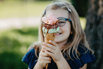 Happy preschool girl eating colorful ice cream in waffle cone on sunny summer day. Little toddler child eat icecream dessert. Sweet food on hot warm summertime days. Bright light, colorful ice-cream.