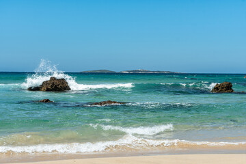 View across beautiful green blue cool clear ocean sea water to a remote island on the horizon waves splashing on the rocks clear blue sky summer holiday destination