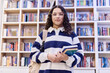 Waist up portrait of young teenage girl wearing glasses standing in school library and holding books with backpack copy space