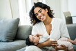 Smiling black mother and beautiful daughter looking at camera sitting on sofa - Portrait of happy african american woman hugging her cute little girl - Family concept
