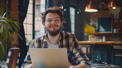 His sweet smile reflects charm as he works on a laptop while he thinks about a problem solution. He's working in a creative, stylish office.
