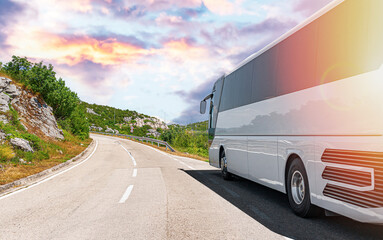 A white tourist bus travels along a picturesque mountain road.