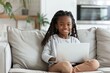 © Marina Demidiuk - Little girl using laptop sitting sofa. Cute little girl using technology device sitting at home alone. Girl playing on phone. One person. Happy elementary age kid rest on couch enjoy weekend