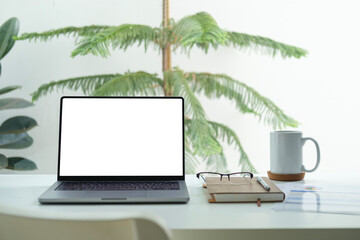 Wall Mural - Laptop computer with blank screen, notepad and cup of coffee on white working desk near window.