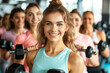© ink drop - A smiling young woman with a group of friends doing dumbbell curls in a gym