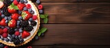 Fototapeta  - Top view of a tart adorned with fresh berries and cookies presented on a wooden background with ample copy space image