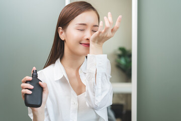 Wall Mural - Perfume of essential aroma, beauty concept. attractive perfect asian young woman holding perfume bottle, using spray and applying fragrance, smelling scent at wrist on body reflect of mirror at home.