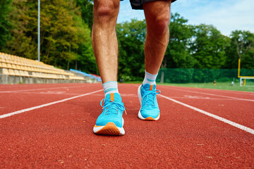 Wall Mural - Athlete wearing bright blue running shoes on red stadium track during training. Sportsman legs in sport sneakers at racetrack. Fitness and healthy lifestyle concept